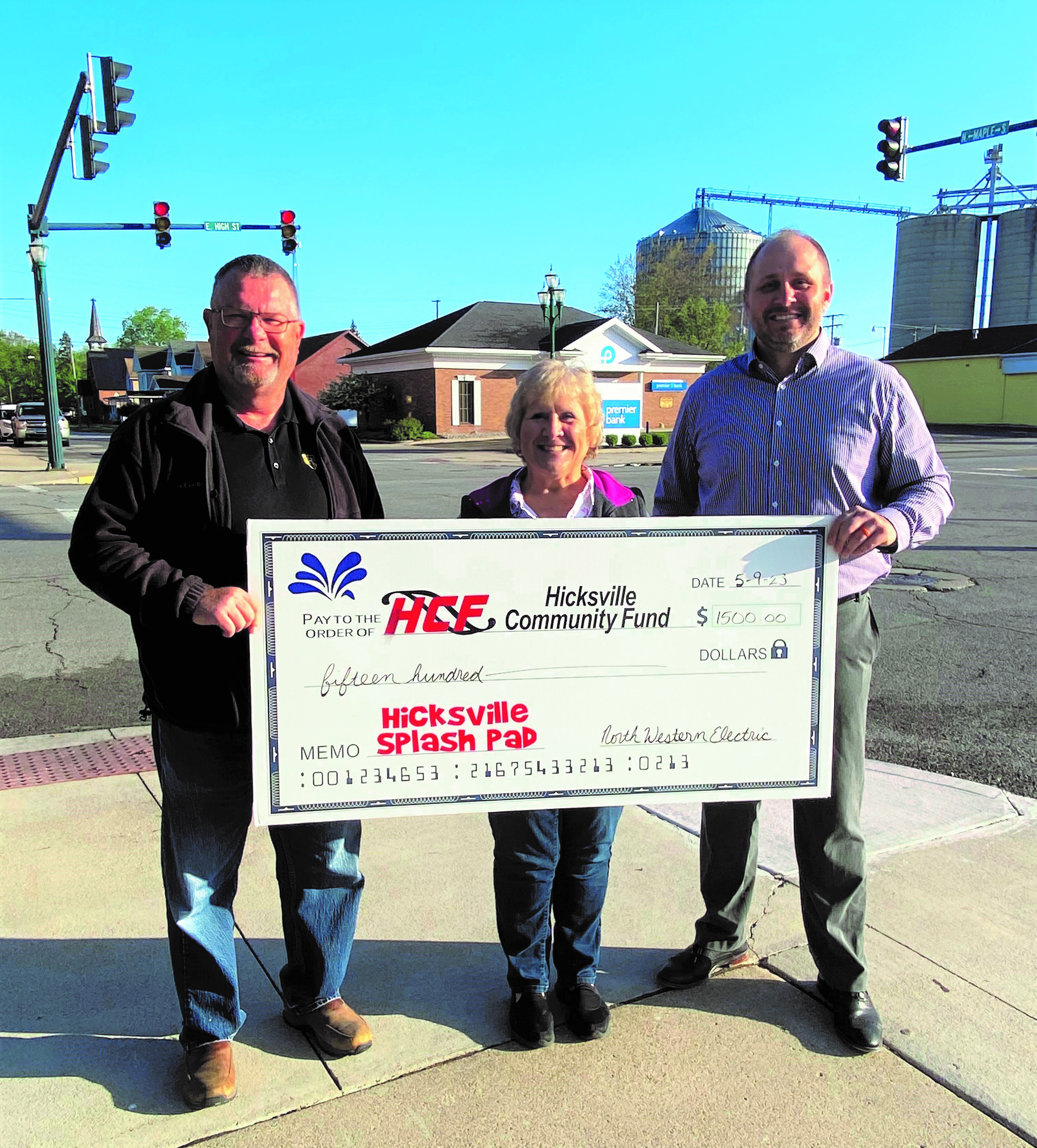 TWO MEN AND ONE LADY HOLDING A BIG CHECK WHILE STANDING ON SIDEWALK