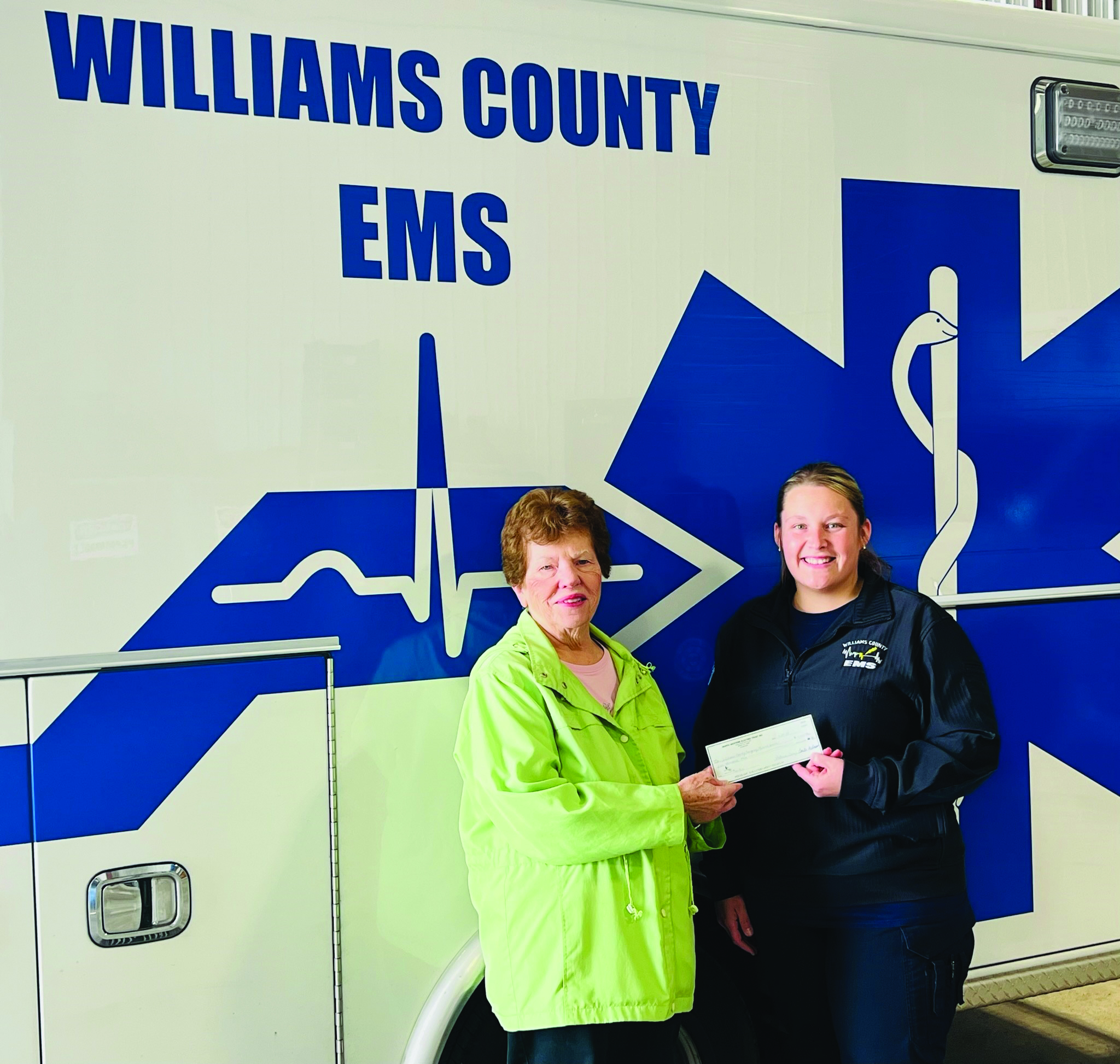 TWO WOMEN STANDING NEXT TO AMBULANCE HOLDING A CHECK