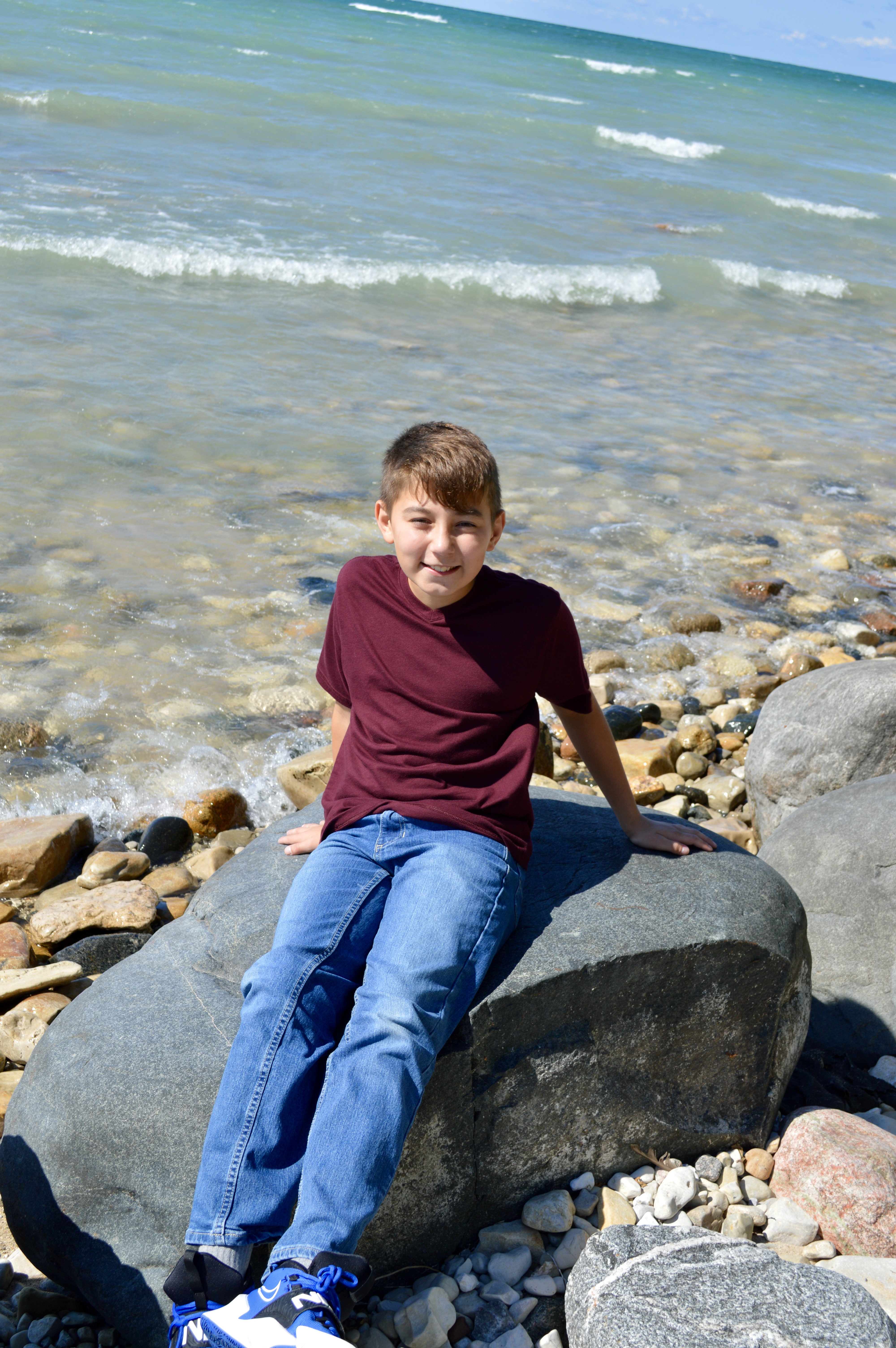 young boy sitting on a rock by a lake